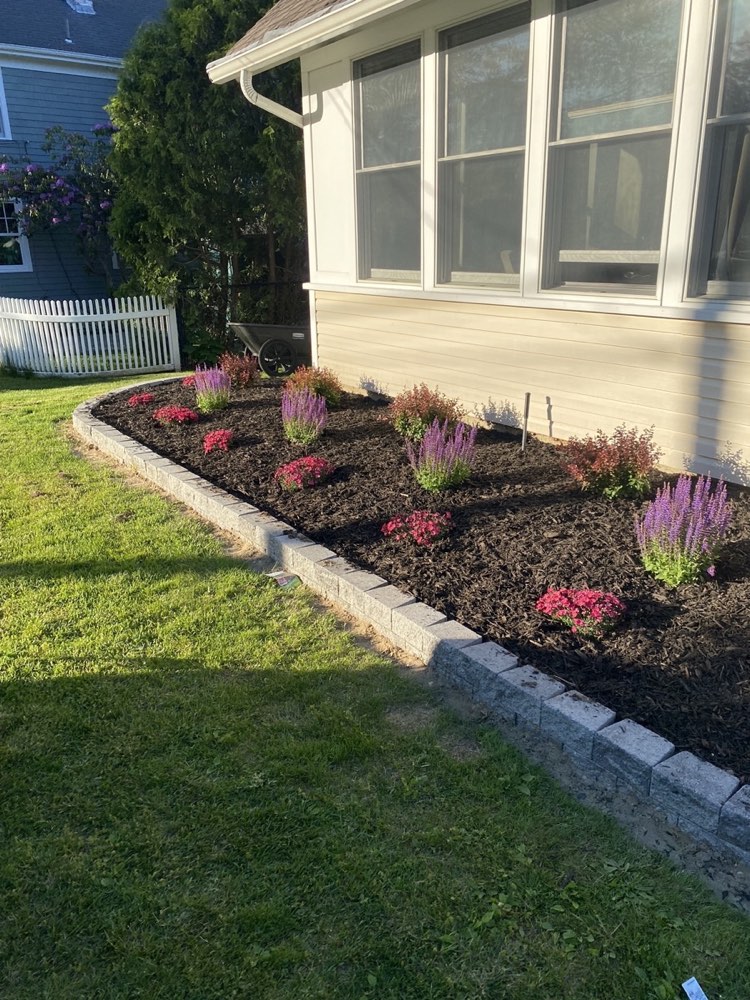 The same bed finished with a curved paver border, fresh mulch, and flowering plants